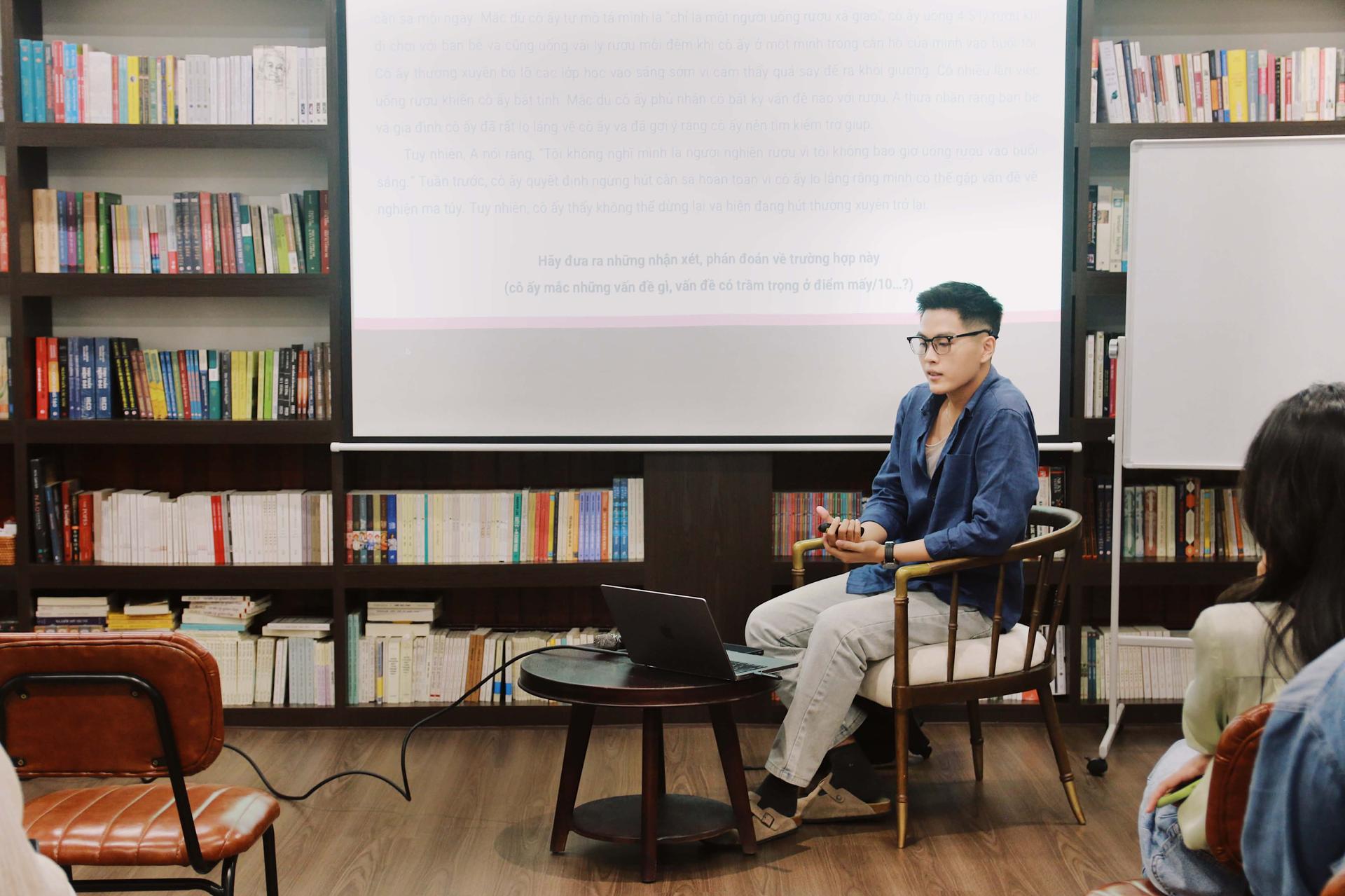 Người trình bày bên chiếc bàn nhỏ, màn chiếu đặt câu hỏi cho cả phòng.