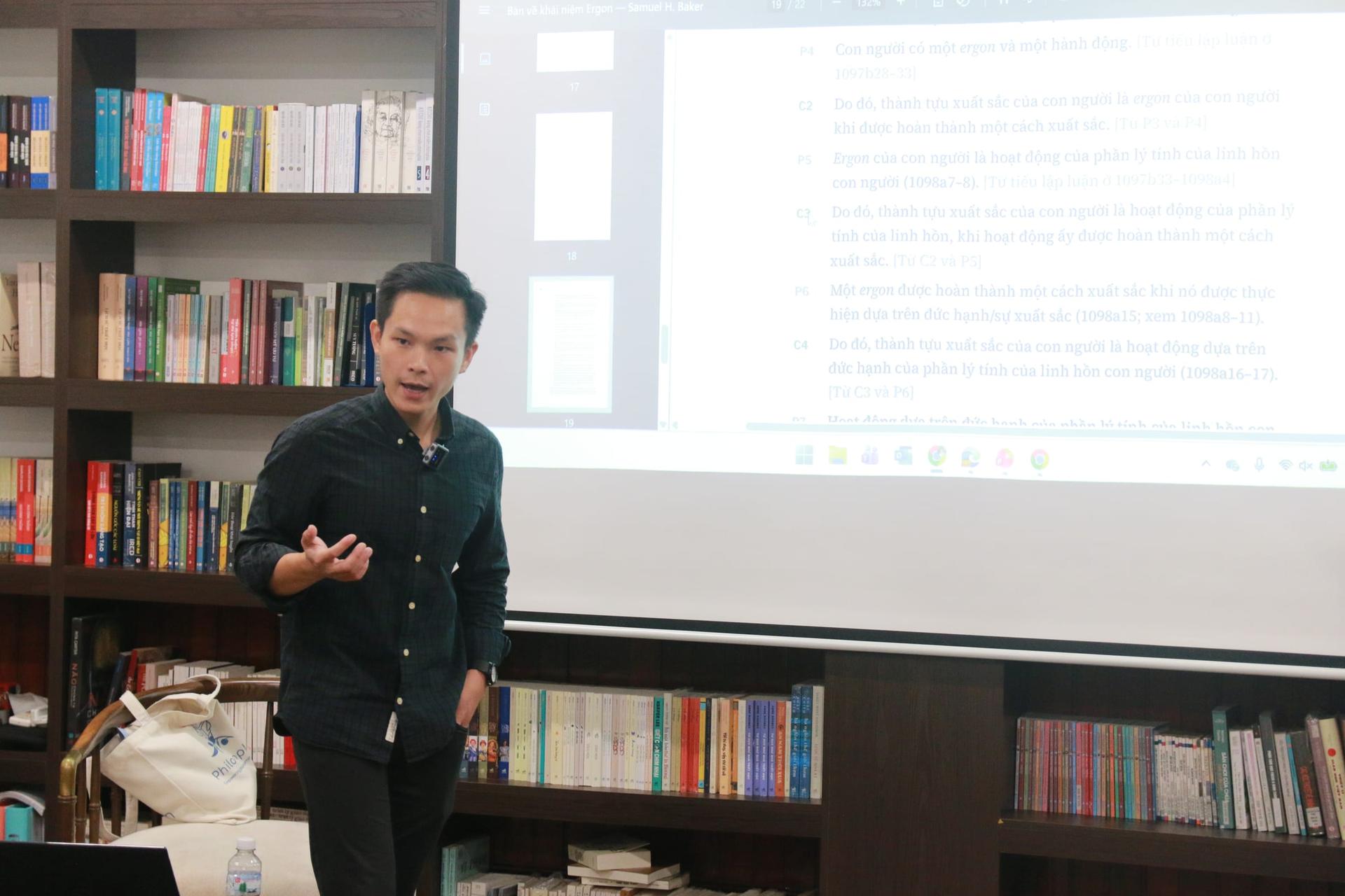 TS Tôn Thất Vĩnh Khang đứng giảng giải, một tay trong túi, tay kia đưa ra, trước màn chiếu các đoạn trích được đánh số.